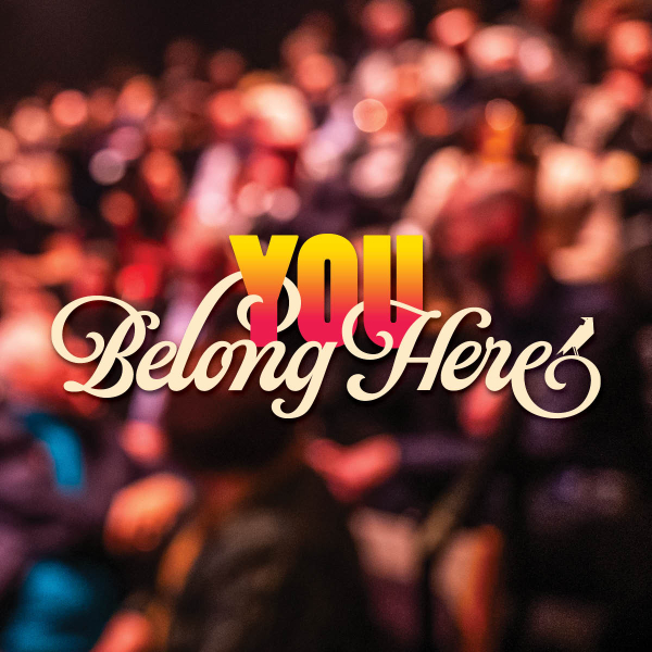 Blurred image of an audience seated in rows, likely in a theatre or auditorium setting, with the words 