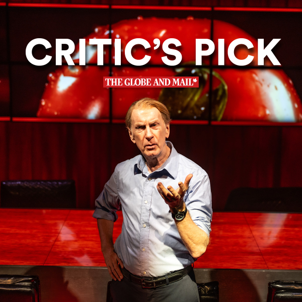 Tom Rooney stands in front of a red table, wearing a light blue dress shirt, dark pants, and a black watch. He gestures with his right hand while his left rests on his hip. Behind him is a large digital screen displaying a close-up image of a red tomato. At the top of the image are bold white words reading “CRITIC’S PICK,” with “THE GLOBE AND MAIL” in smaller red text below it. Four empty chairs are partially visible around the table.