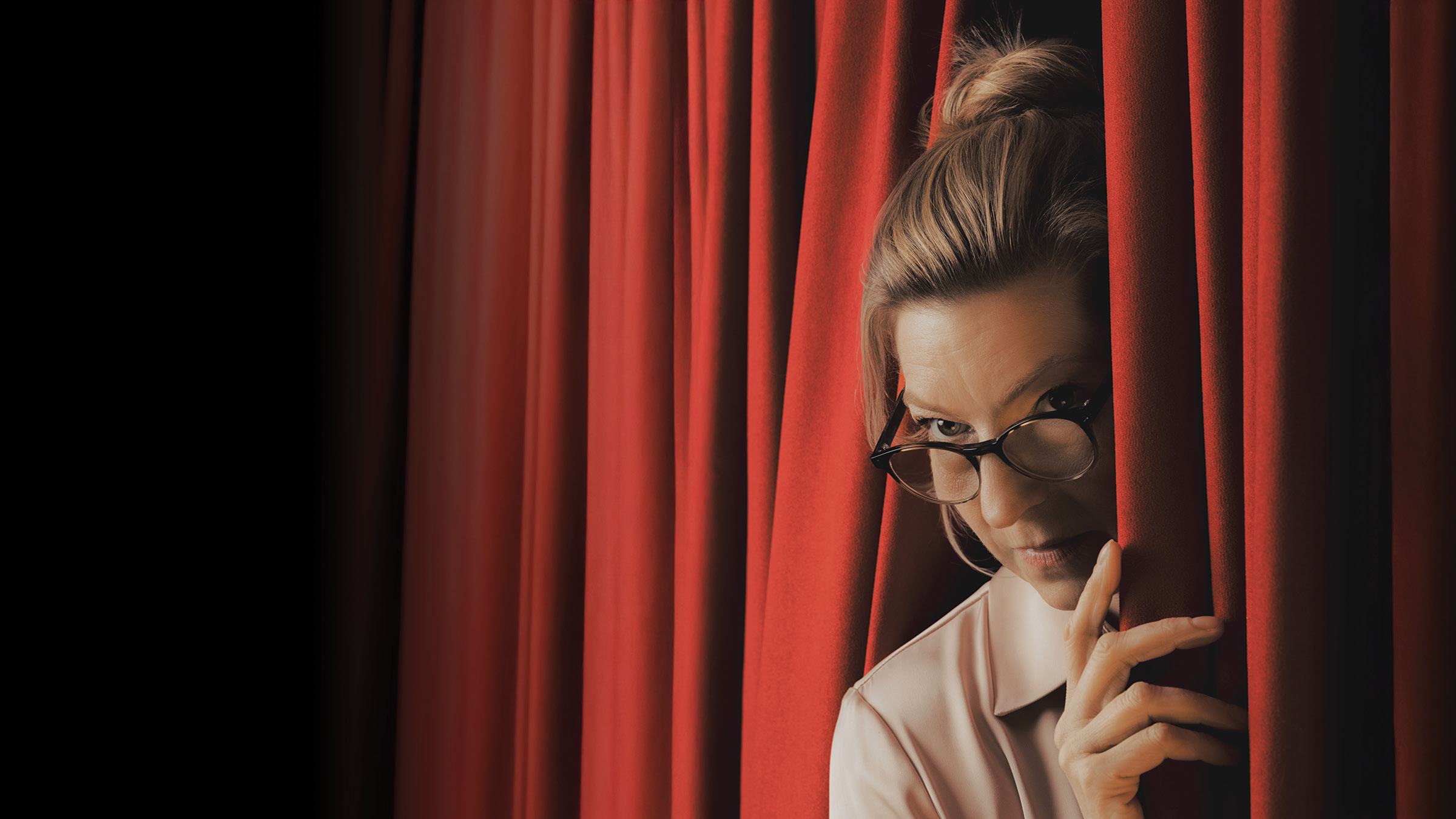 A woman peeking out from a red curtain